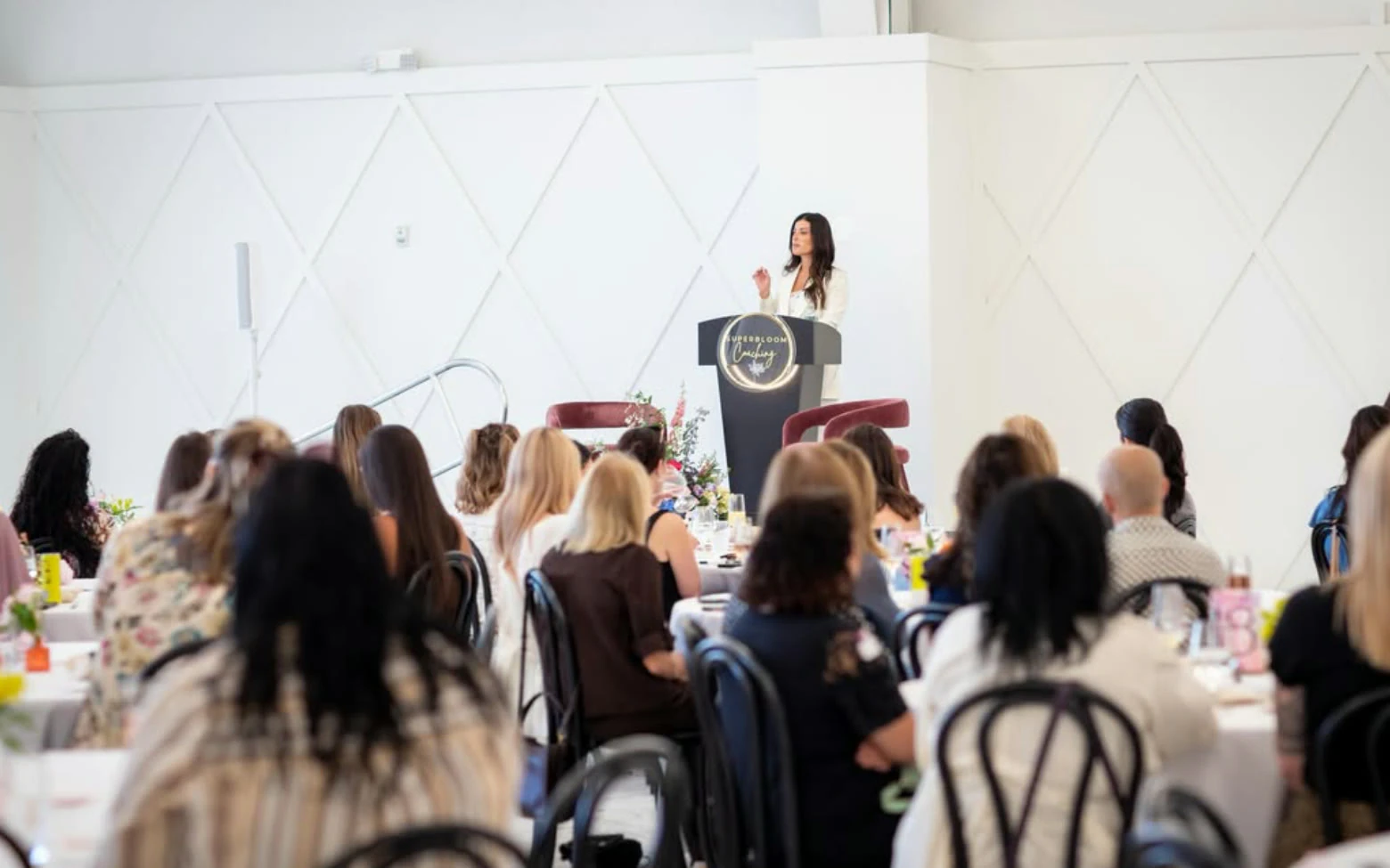 Alana speaking at a Superbloom Coaching podium to a full room of women.