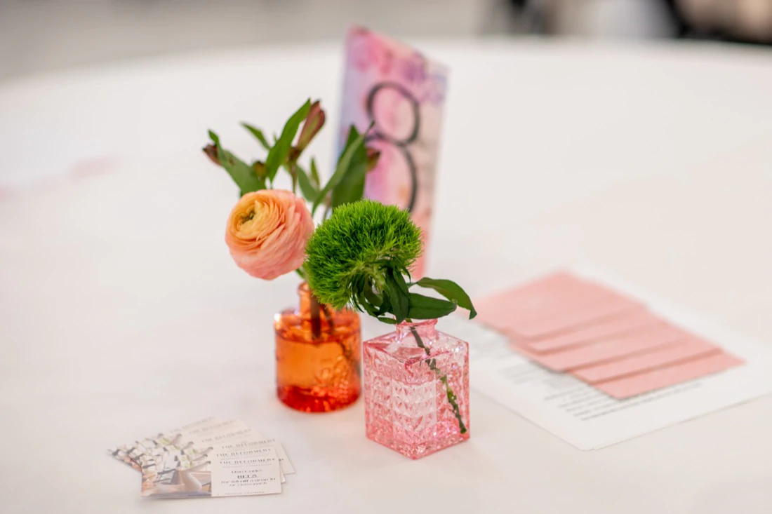 Table flowers in orange and pink bud vases beside a table number.