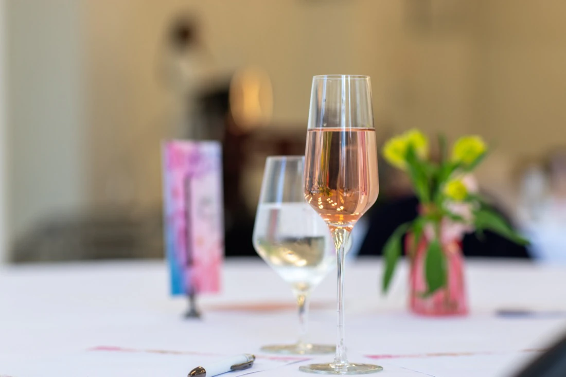 A glass of ros&eacute; on a table setting, the stage soft in the background.